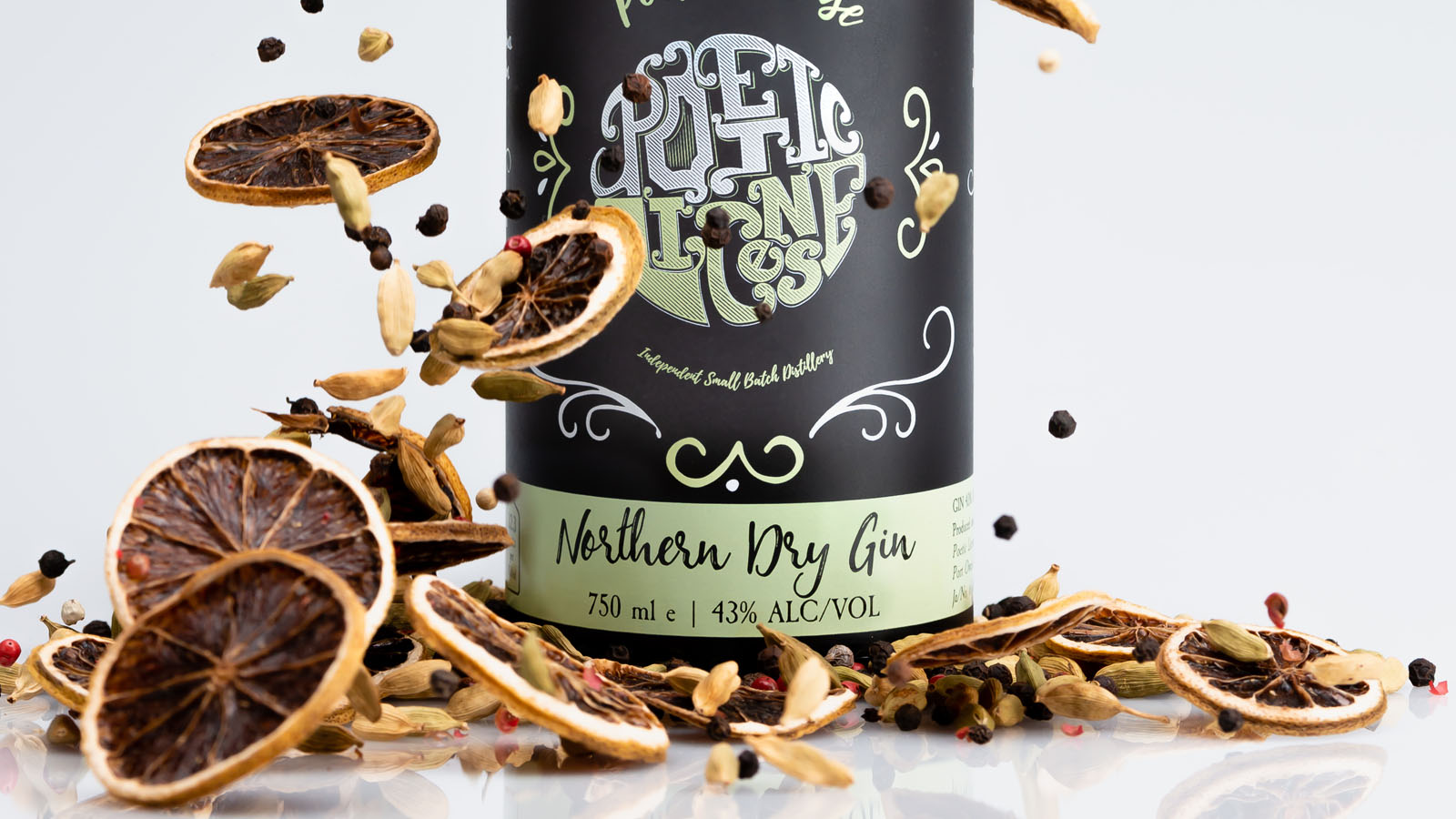 Close-up of gin bottle with botanicals falling around it.