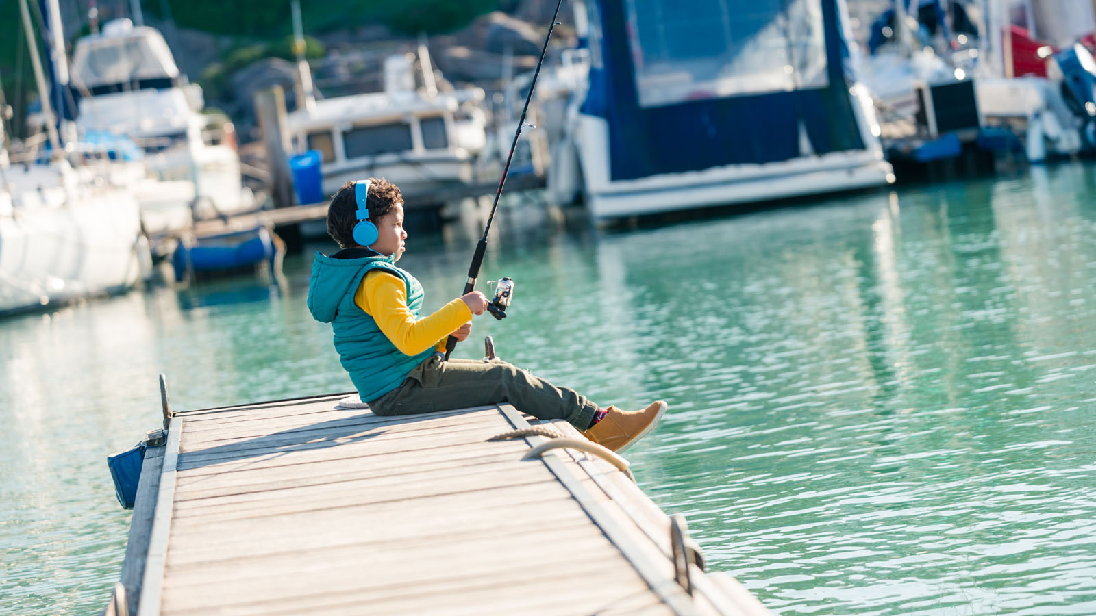 Young boy with headphones fishing from quayside.