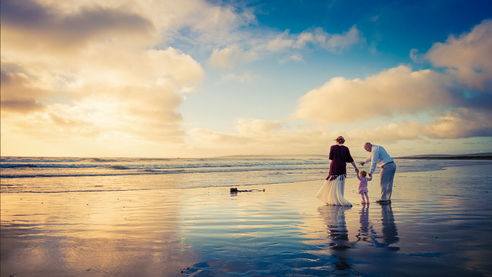 Family admiring the cloudscape on beach at low tide.